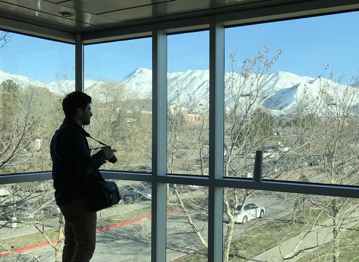 A photographer stands silhouetted against large windows through which can be seen the snow-capped mountains surrounding Utah.
