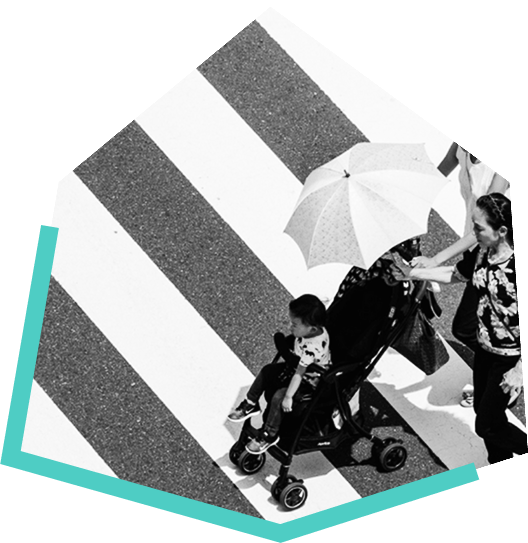 Two women crossing a cross walk, one holding an umbrella, and the other pushing a baby in a stroller.