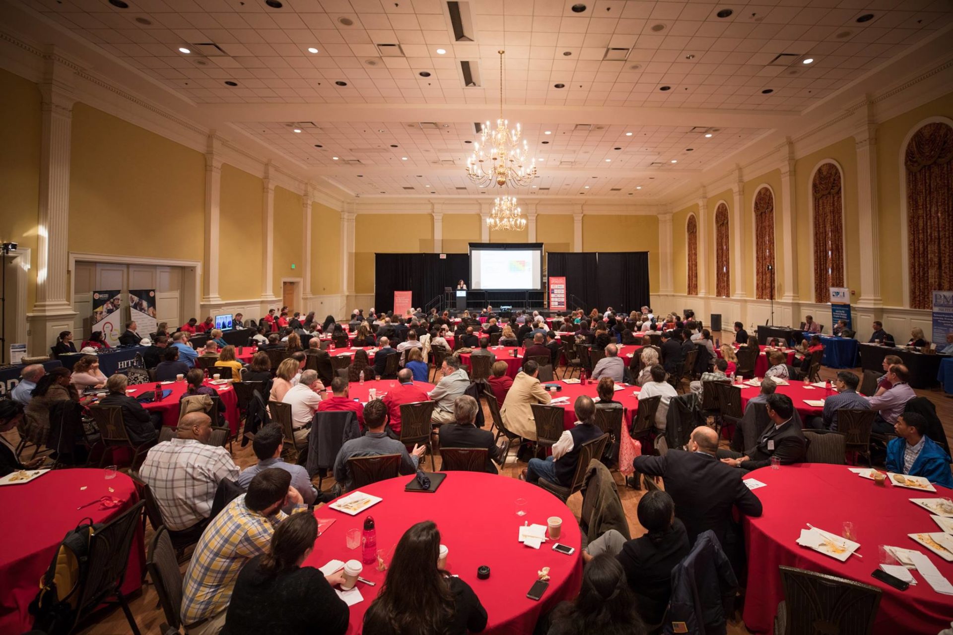 Round tables with red tablecloths in the main ballroom of the 2017 UMD PM conference with participants seated around each table.