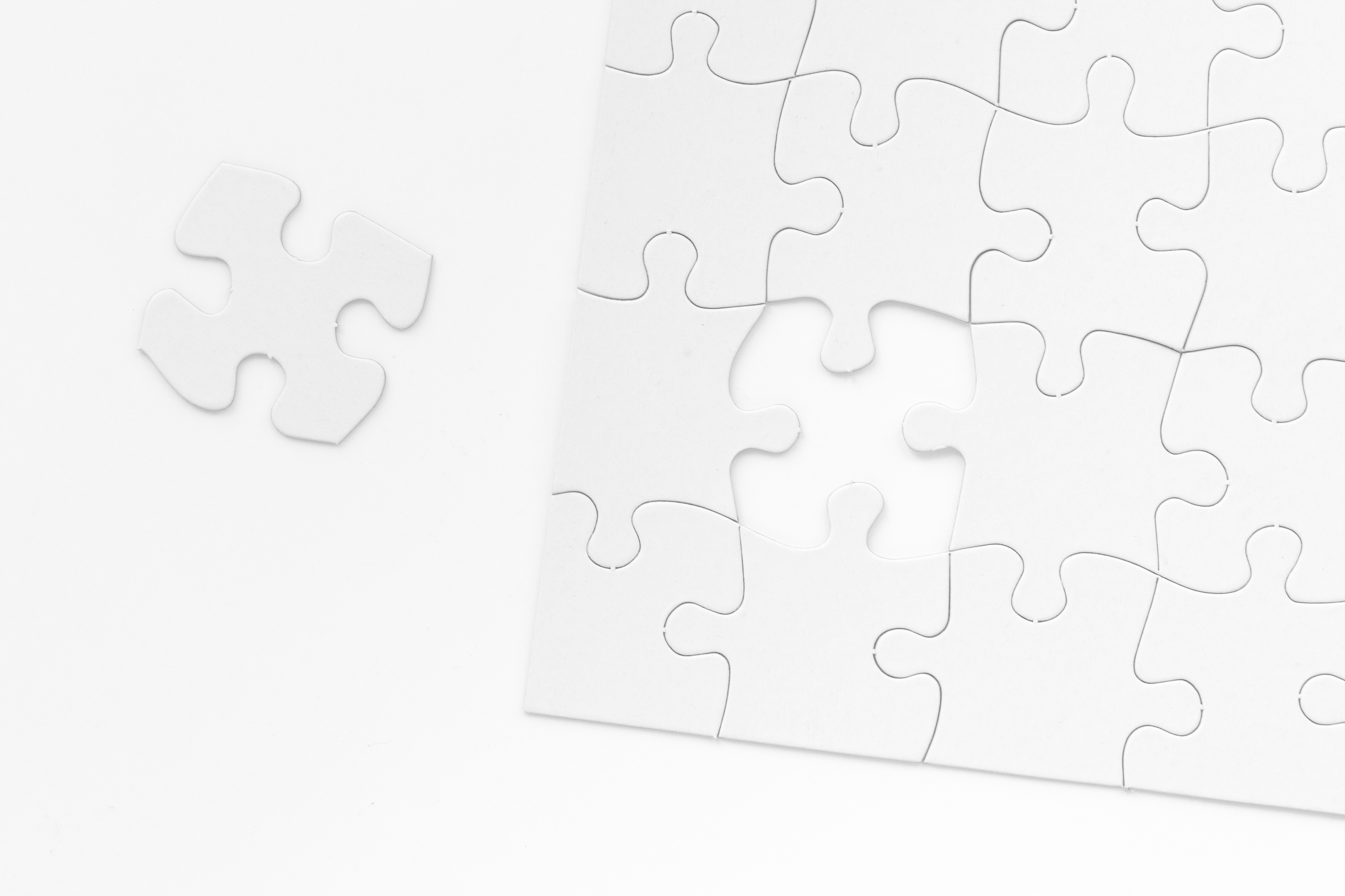 A black and white image of a puzzle missing a singular piece. The remaining piece is seen to the left of the puzzle