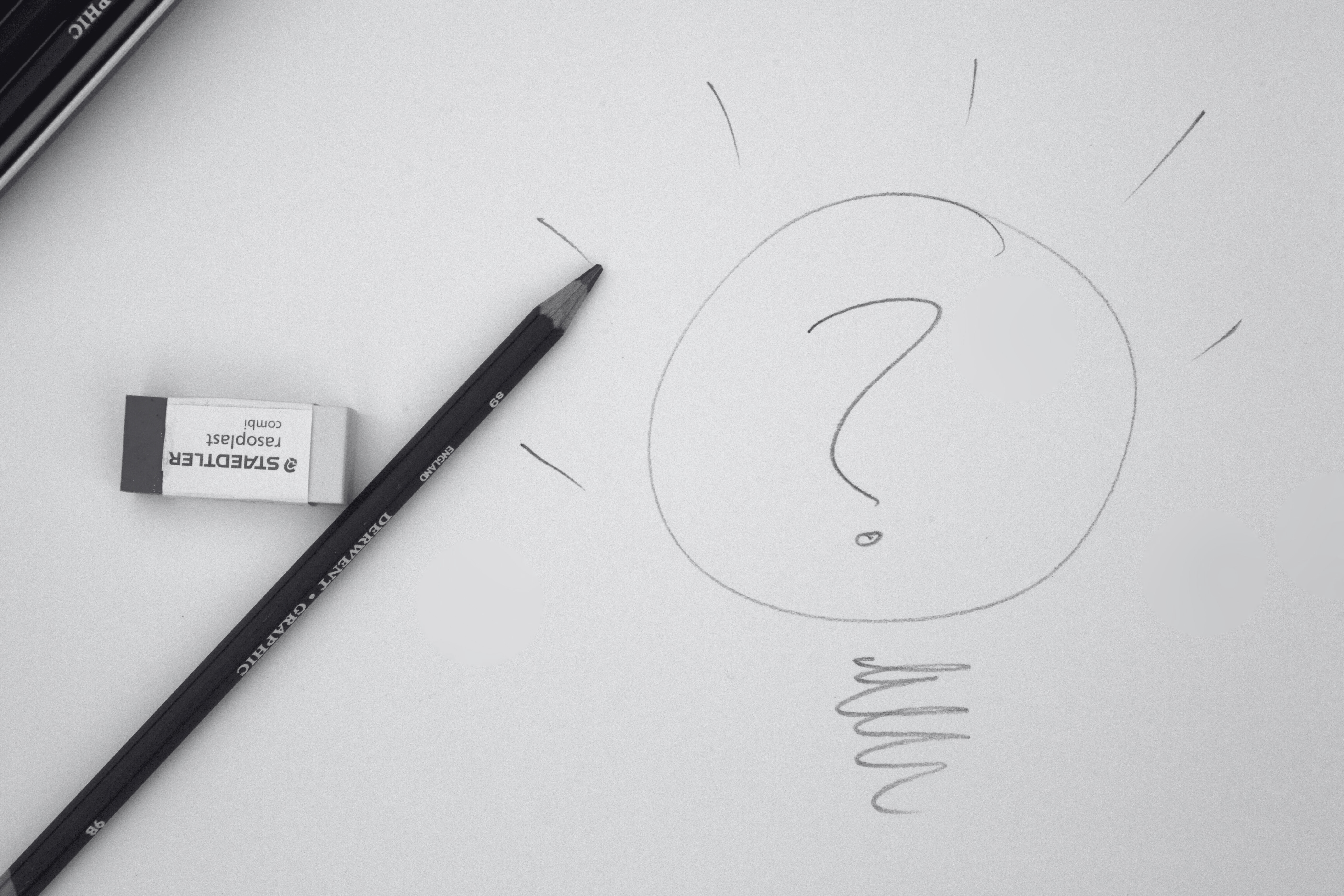 black and white image of a pencil and a drawing of a question mark inside a light bulb.