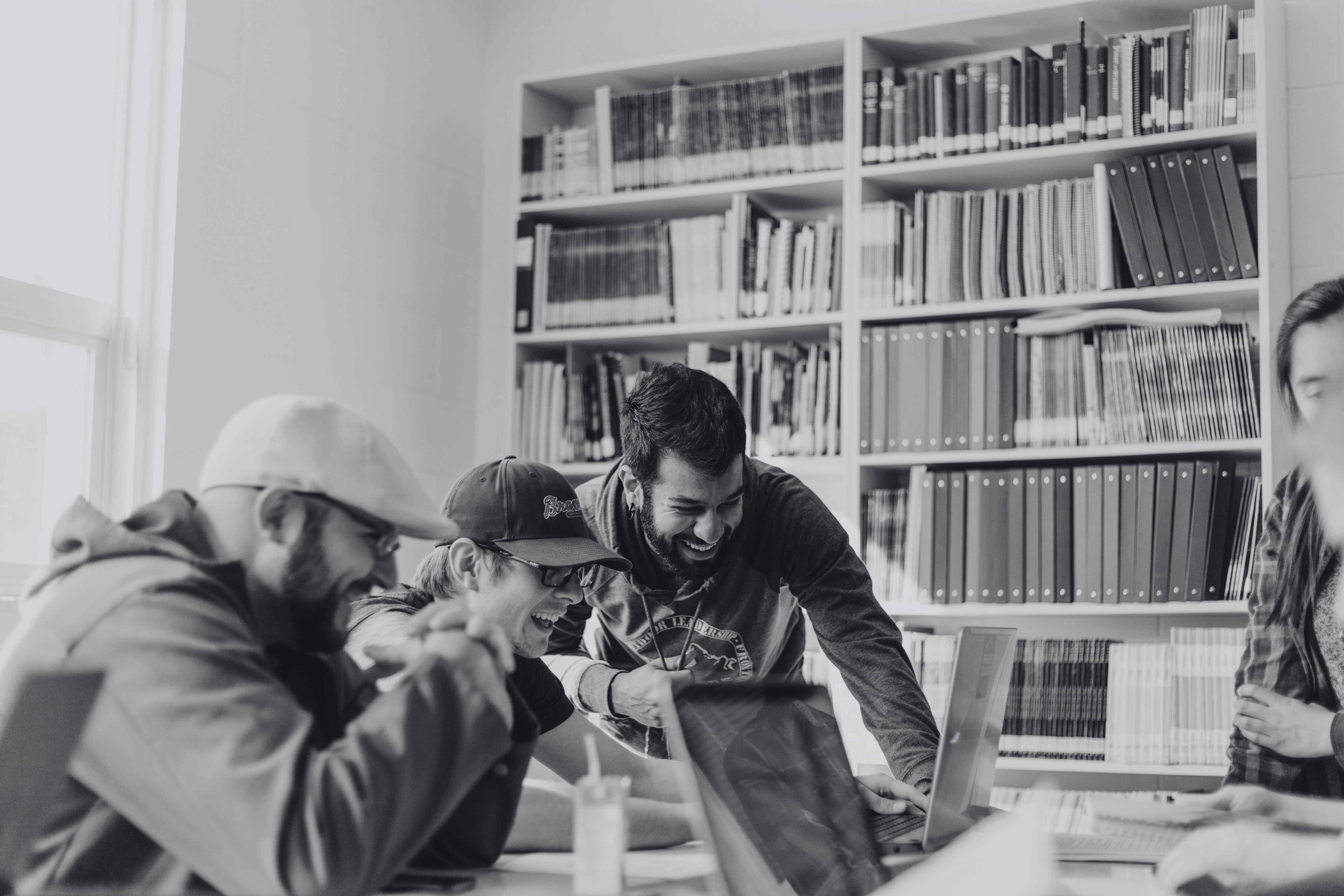 A black and white photo of a group of people huddled around a laptop at a library.
