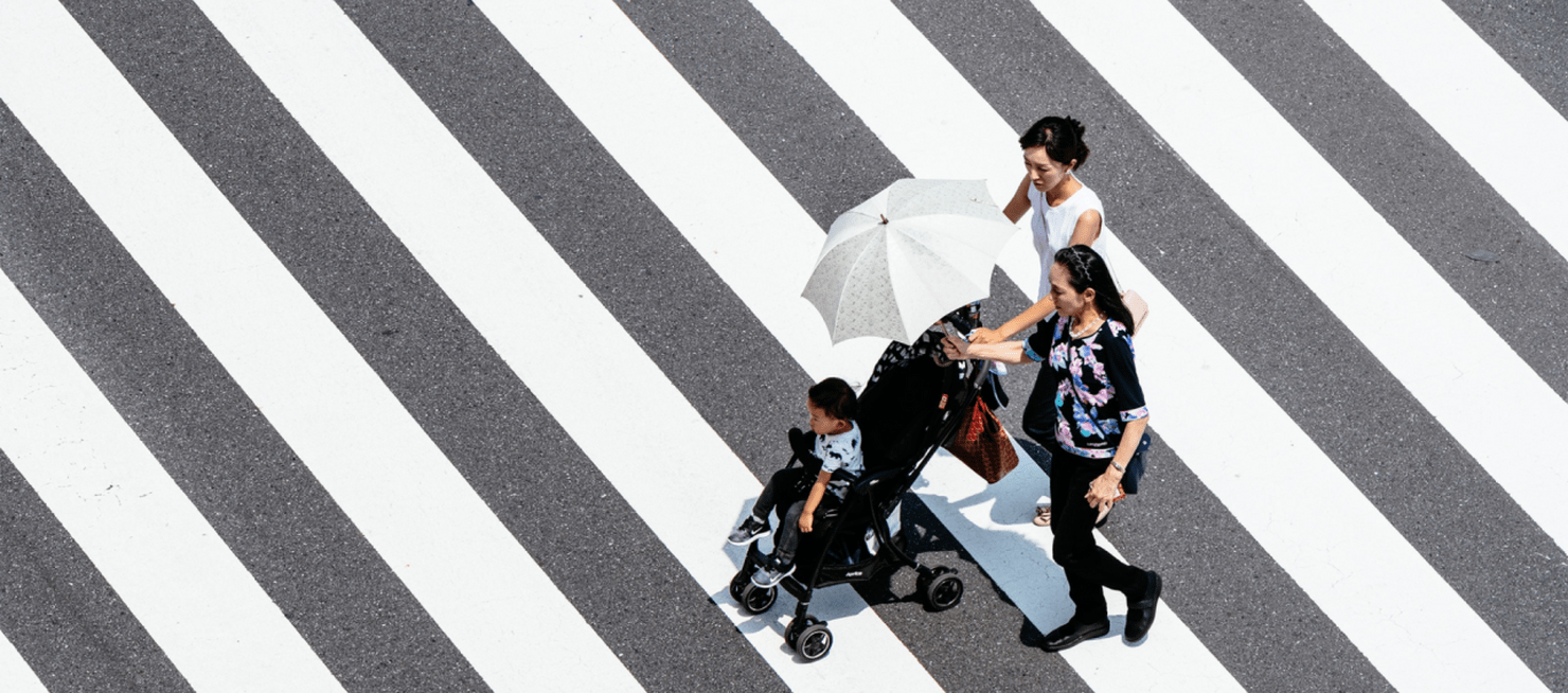 a family pushing a toddler in a stroller crossing a sidewalk