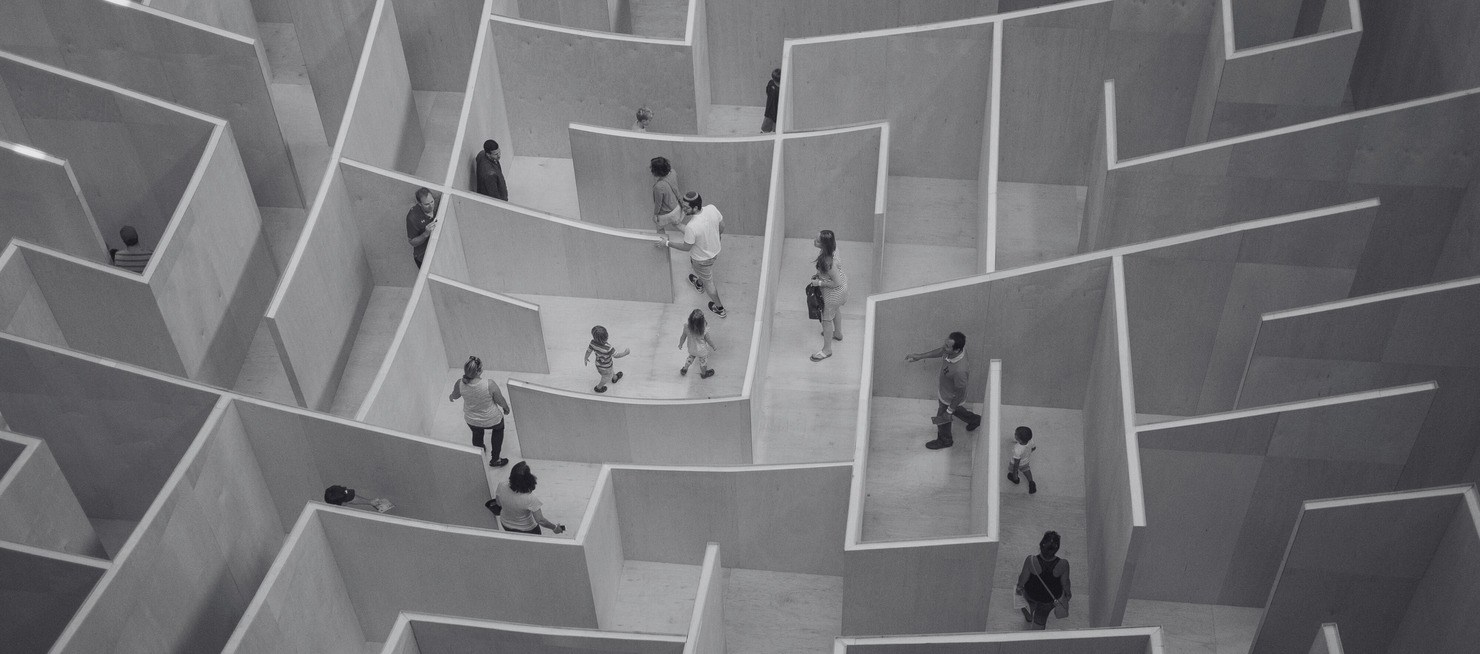 People walking through a large indoor wooden maze with high walls, seen from above.