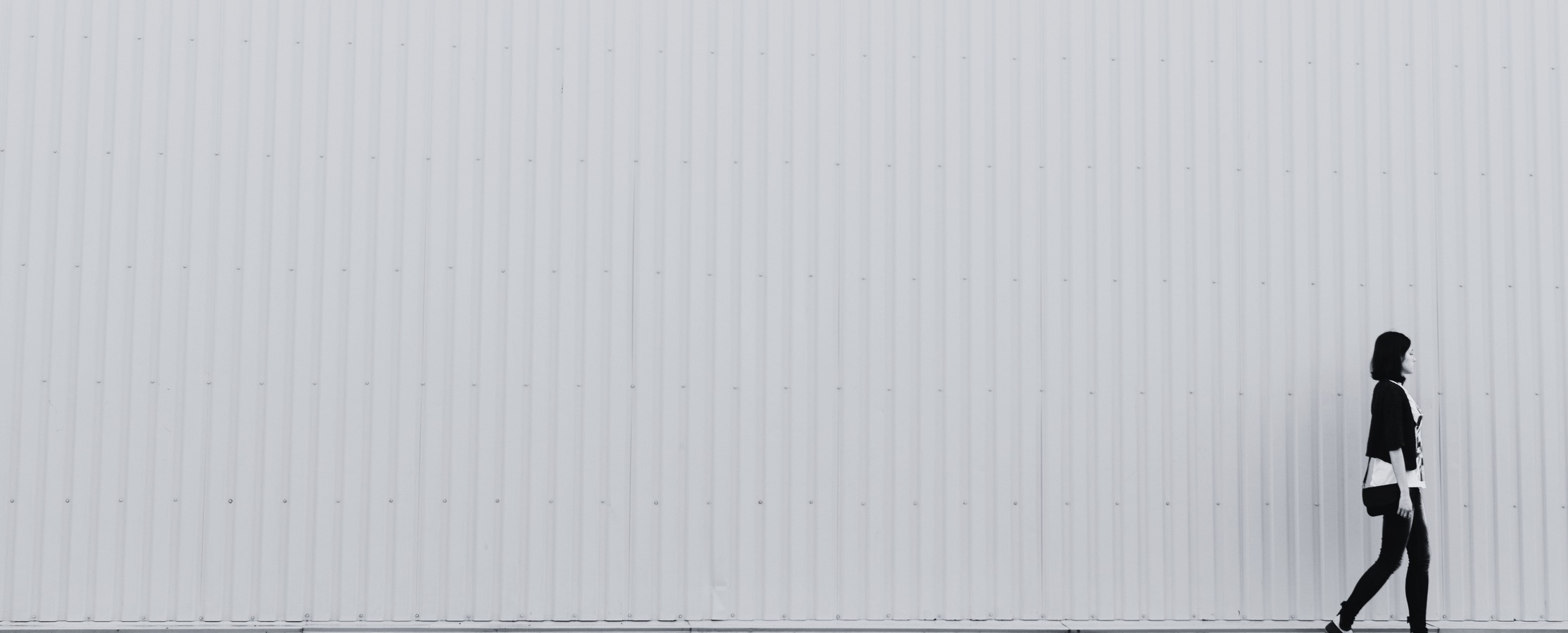 Black and white photo of a woman walking against a blank wall