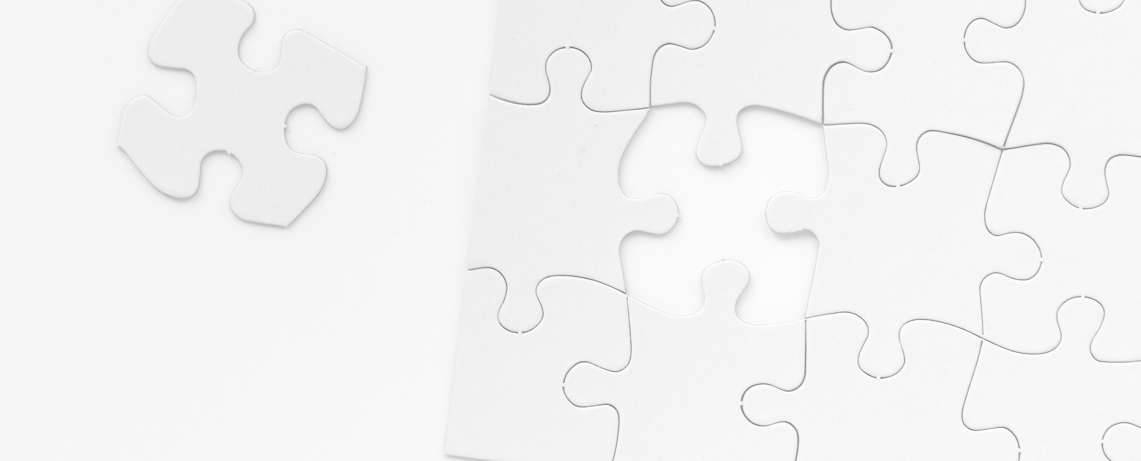 A black and white image of a puzzle missing a singular piece. The remaining piece is seen to the left of the puzzle