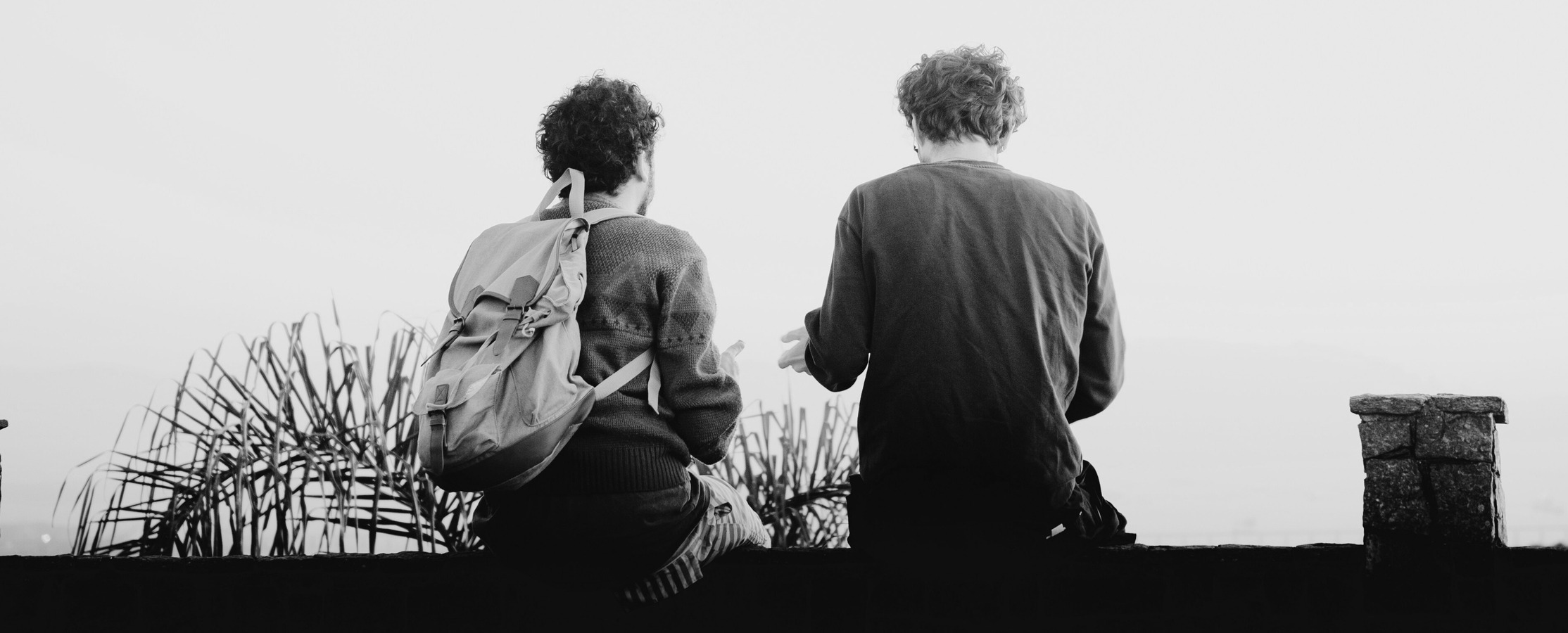 A black and white photo of two people sitting on a ledge.