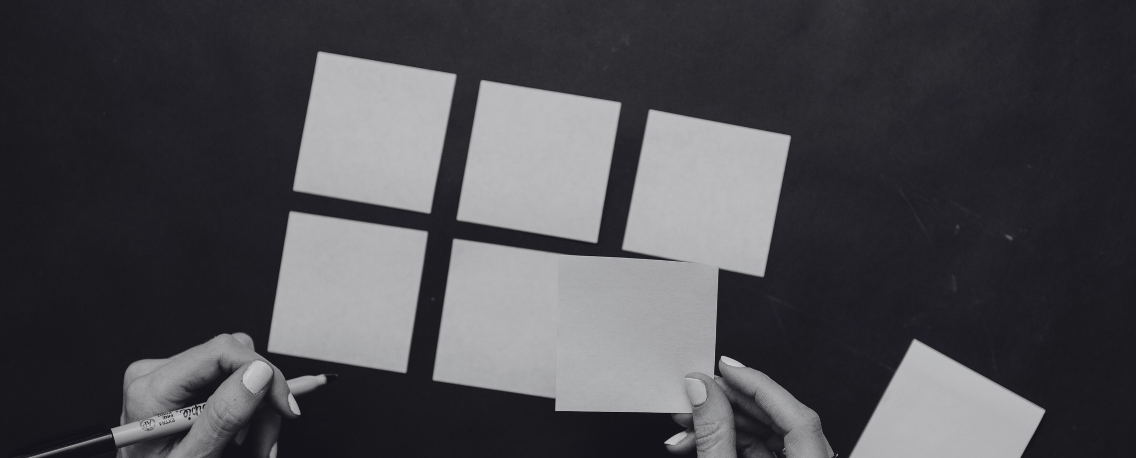 Hands arranging blank sticky notes into a grid on a dark surface, shown in black and white