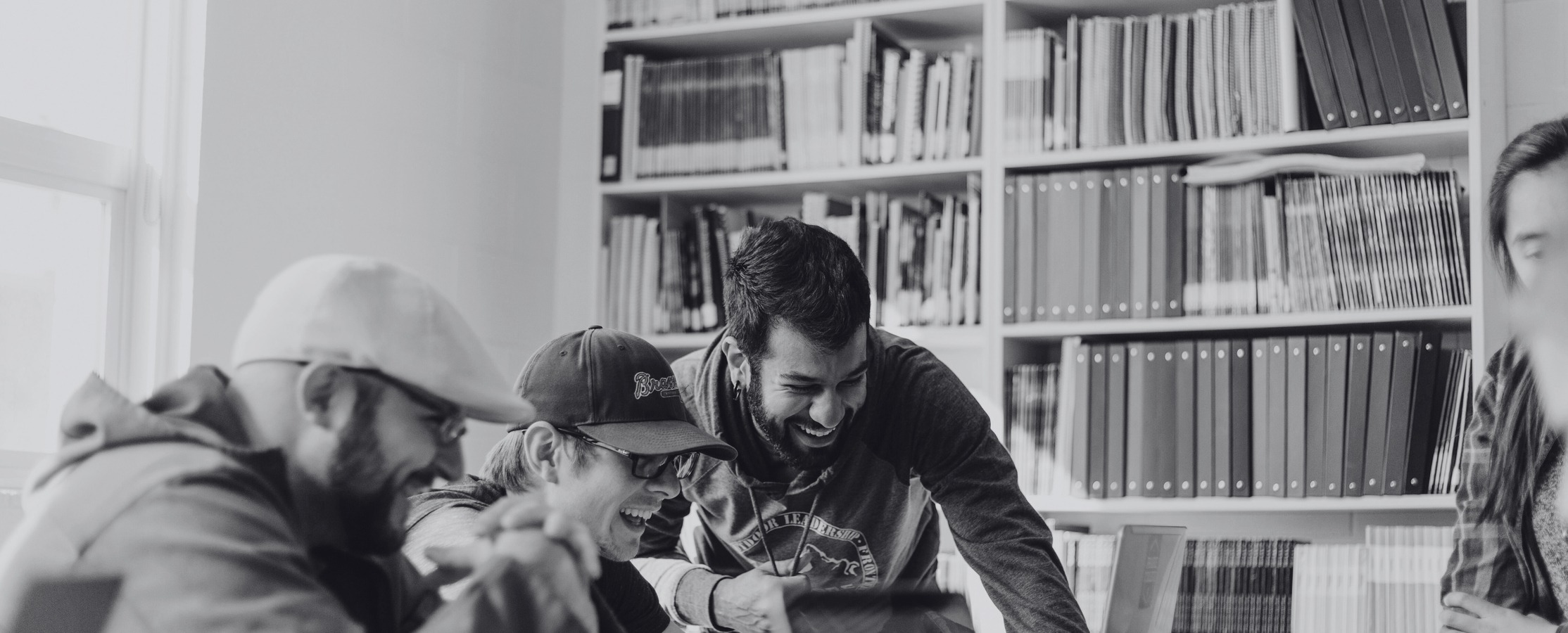 A black and white photo of a group of people huddled around a laptop at a library.