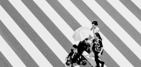a family pushing a toddler in a stroller crossing a sidewalk