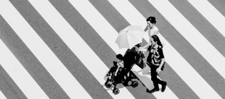 a family pushing a toddler in a stroller crossing a sidewalk