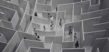 People walking through a large indoor wooden maze with high walls, seen from above.