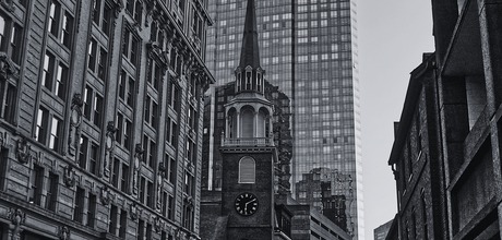 Black and white historic brick church steeple with clock tower framed by modern glass skyscraper and historic buildings in downtown Boston
