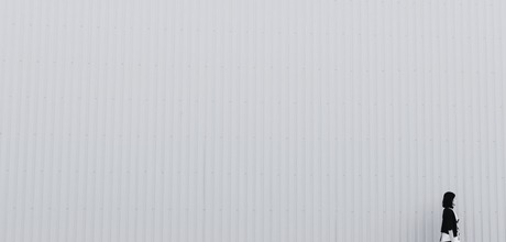 Black and white photo of a woman walking against a blank wall