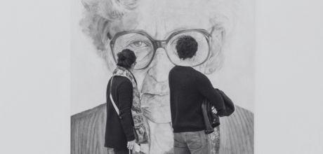 A man and woman walk through a modern art museum, viewing a large black and white portrait of an elderly woman with glasses.