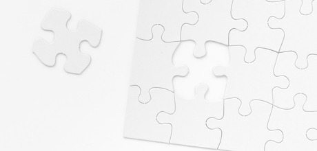 A black and white image of a puzzle missing a singular piece. The remaining piece is seen to the left of the puzzle