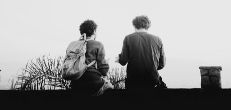 A black and white photo of two people sitting on a ledge.