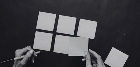 Hands arranging blank sticky notes into a grid on a dark surface, shown in black and white