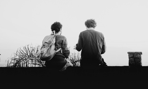A black and white photo of two people sitting on a ledge.