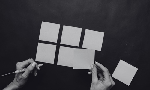 Hands arranging blank sticky notes into a grid on a dark surface, shown in black and white