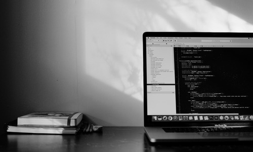 A black and white image of a laptop showing code on the screen