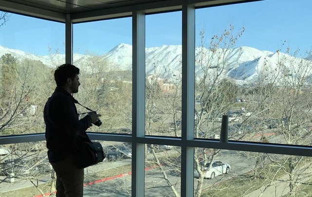 A photographer stands silhouetted against large windows through which can be seen the snow-capped mountains surrounding Utah.