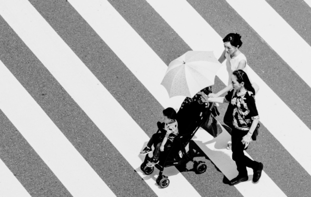a family pushing a toddler in a stroller crossing a sidewalk