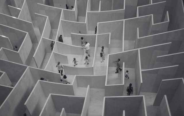 People walking through a large indoor wooden maze with high walls, seen from above.