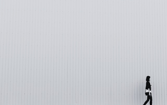 Black and white photo of a woman walking against a blank wall