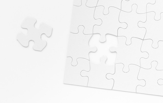 A black and white image of a puzzle missing a singular piece. The remaining piece is seen to the left of the puzzle