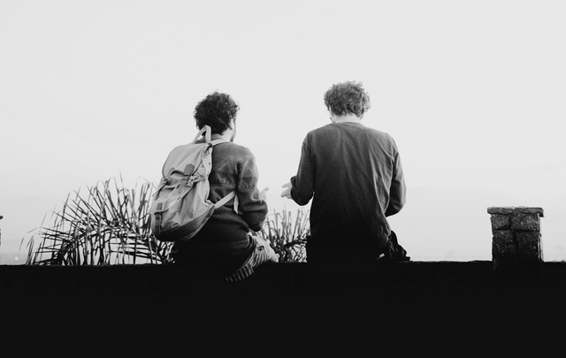 A black and white photo of two people sitting on a ledge.