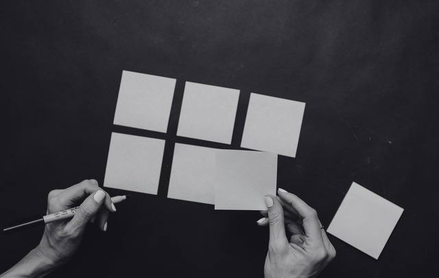 Hands arranging blank sticky notes into a grid on a dark surface, shown in black and white