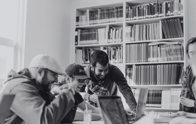 A black and white photo of a group of people huddled around a laptop at a library.