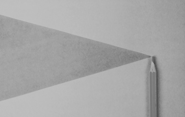 Gray pencil on white paper casting a triangular shadow.