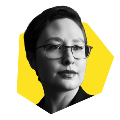 Headshot of Cori, a white woman with glasses and short hair, in a yellow polygon shape