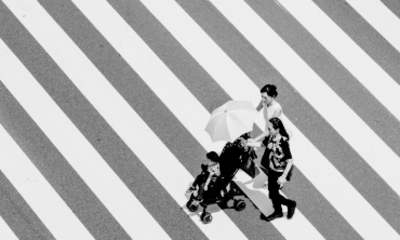 a family pushing a toddler in a stroller crossing a sidewalk