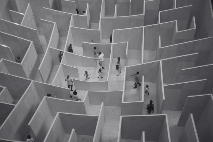 People walking through a large indoor wooden maze with high walls, seen from above.